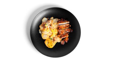 Peynirli fırında patates ve siyah tabakta domuz eti. Beyaz arka planda izole edilmiş..