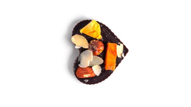 Çiğ kalp şeklinde çikolata, beyaz arka planda kurutulmuş meyve ve fındık..