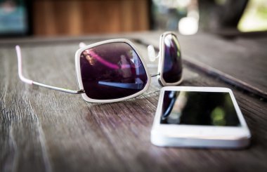 Smartphone ve ahşap masa üzerinde güneş gözlüğü