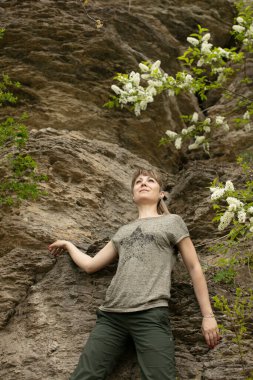 Uzun saçlı genç bir kızın portresi dağların ve ağaçların arka planında, aşağıdan çekilmiş.