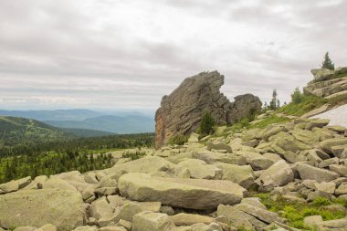 Büyük kurum taşları dağlardaki ormanda, yosunlarla kaplı kayalar ormanın arka planında, dağ manzarasında, yüksek dağlarda yatar...