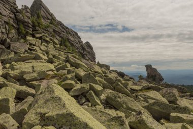 Büyük kurum taşları dağlardaki ormanda, yosunlarla kaplı kayalar ormanın arka planında, dağ manzarasında, yüksek dağlarda yatar...