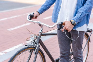 Eski tarz şehir bisikleti, şehirde bisiklet yolunun yanında tanınmayan, günlük kıyafetler giyen beyaz bir adam tarafından tutuluyor.