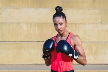 Çekici bir Afrikalı kadının yatay portresi. Spor kıyafetler ve boks eldiveni giymiş. Savunma pozisyonunda duruyor.