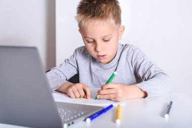Sarışın, beyaz, küçük bir çocuk. 5 yaşında. Oturma odasında keçeli kalemler çiziyor.