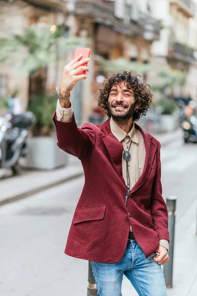 Beyaz tenli çekici bir adam sokakta selfie çekiyor.