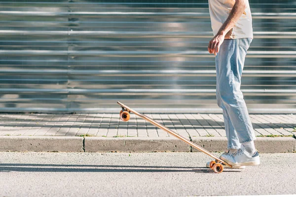 Nerozeznatelný muž s ležérní oblečení zvedání skateboard s nohama — Stock fotografie