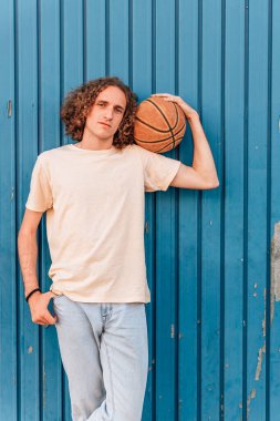 Çekici ve genç kızıl saçlı bir adam elinde mavi arka planlı bir basketbol topu tutuyor.