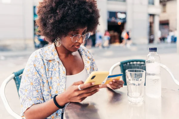 Kredi kartı ve telefonuyla online alışveriş yapan Afro-Amerikalı genç bir kadın.