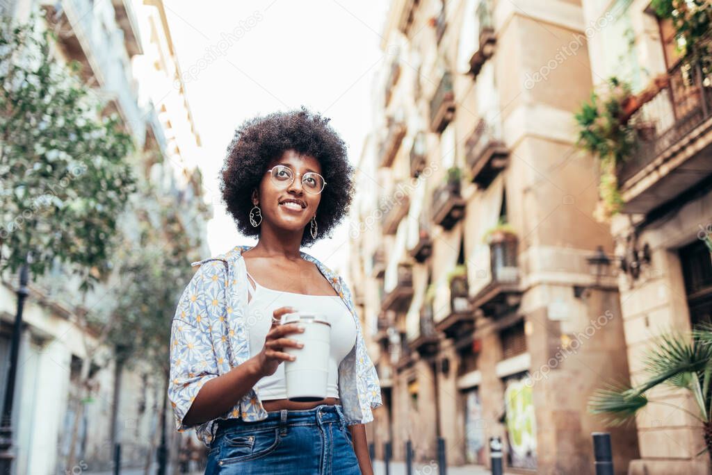 portrait of cheerful african woman walking the streets with a reusable white cup of coffee