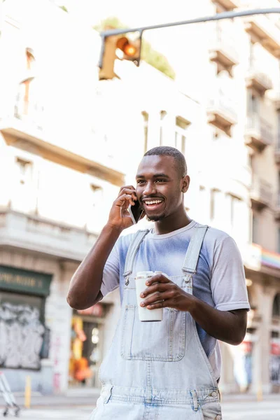 Африканський молодий чоловік з чашкою кави і розмовляє по телефону на вулицях Барселони — стокове фото