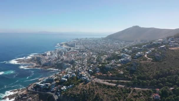 Aérea moviéndose a lo largo de la costa de Camps Bay, Ciudad del Cabo, Sudáfrica, con las montañas de los Doce Apóstoles. — Vídeos de Stock