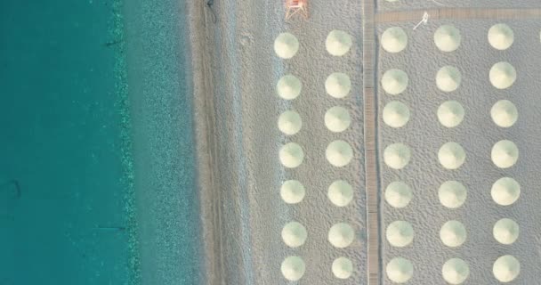 Concepto de vacaciones de verano. Vista desde arriba, impresionante vista aérea de una playa increíble con sombrillas de playa y agua turquesa clara. Vista superior de una tumbona bajo un paraguas en la playa de arena. — Vídeo de stock