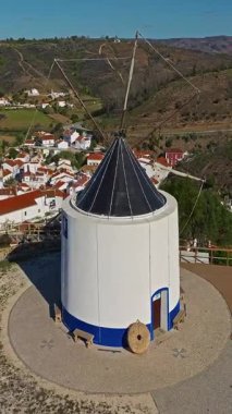  Yel değirmeni ve pitoresk çatıları olan küçük köyün havadan görünüşü, Aldatmaca, Portekiz.