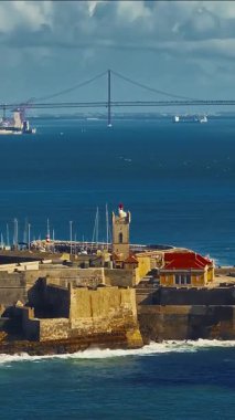  Arka planda ünlü bir köprü olan Portekiz 'deki bir kalenin insansız hava aracı görüntüsü. Portekiz, Carcavelos sahilinden deniz feneri kulesi olan Aziz Julian Kalesi. Carcavelos 'taki Atlantik okyanus dalgaları plajı.