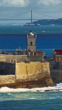  Arka planda ünlü bir köprü olan Portekiz 'deki bir kalenin insansız hava aracı görüntüsü. Portekiz, Carcavelos sahilinden deniz feneri kulesi olan Aziz Julian Kalesi. Carcavelos 'taki Atlantik okyanus dalgaları plajı.