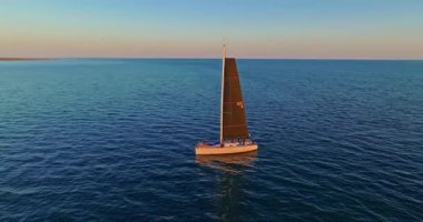 Siyah yelkenli sinematik yelkenli açık denizde yelken açan batan güneşin ışınlarıyla yıkanan ve günbatımı atmosferindeki sakin suları ortaya çıkaran. Macera ve rahatlama kavramı.