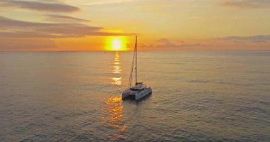 Gün batımında sakin denize demirlenmiş katamaranın havadan görünüşü.