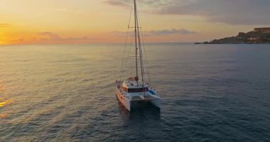 Gün batımında sakin denize demirlenmiş katamaranın havadan görünüşü.