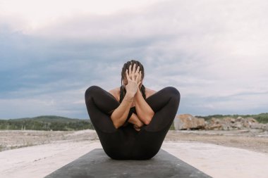 Siyah takım elbiseli yogacı kız gün batımında yoga egzersizleri yapıyor.