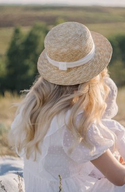 Hasır şapkalı kız tarlada oturuyor.