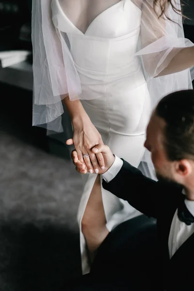 The groom in a suit holds the hand of the bride