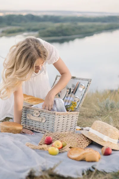Kız ve piknik seti bulaşık, ekmek, meyve ve şapkayla nehir kıyısında