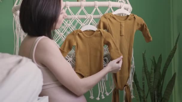 Молодая Беременная Девушка Вешает Детскую Одежду Кроватку Игрушками — стоковое видео