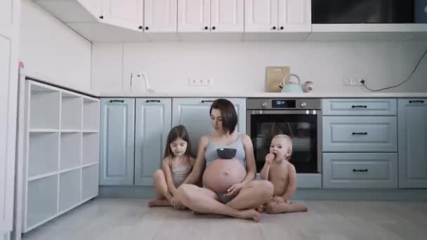 穿着蓝色内裤 两个小孩在厨房里吃着燕麦片的年轻怀孕女孩 — 图库视频影像