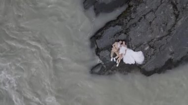 Gelin ve damat Altai 'deki dağların arka planında nehir kıyısında gelinlik giymişler.