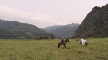 Gelinlikli gelin ve damat Altai 'deki dağların arasında ata biniyor.