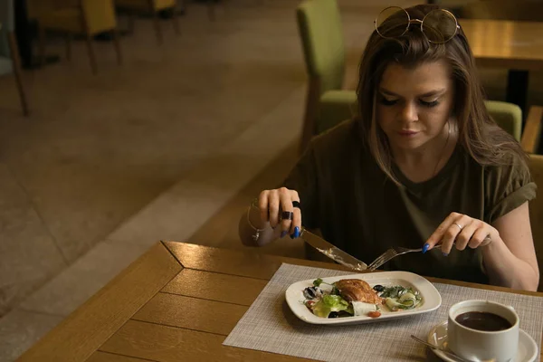 Ung vacker kvinna äter frukost på caféet. Vacker ung kvinna äter frukost med croissant med kyckling, grönsaker och sallad och kaffe på café — Stockfoto