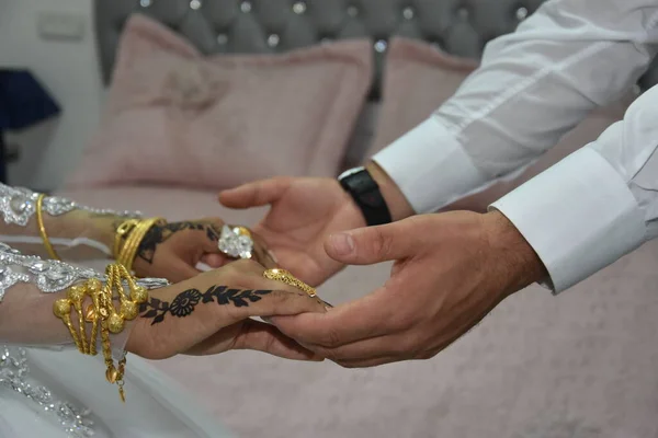 Mãos de recém-casados, juntamente com anéis de ouro do casamento perto da cama de casamento de recém-casados — Fotografia de Stock