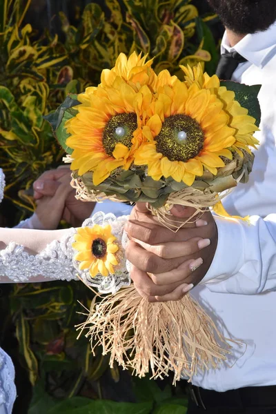 the bride\'s hands with gold rings are holding a bouquet of yellow sunflower flowers. High quality photo