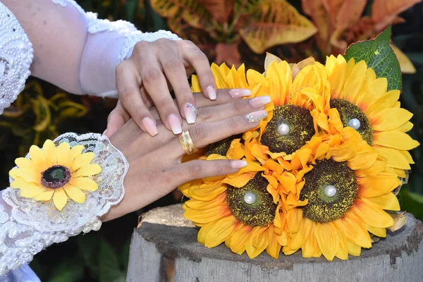 the bride\'s hands with gold rings lie on a bouquet of yellow sunflower flowers. High quality photo