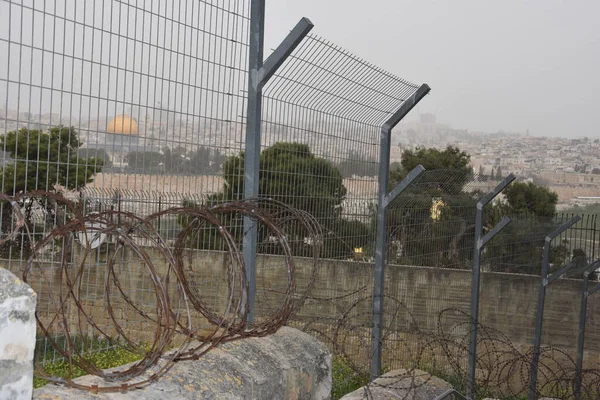 Jerusalem, Israel. Metal wire fence along a brick wall, view of the Al Aqsa Mosque with a golden dome in the distance. High quality photo. 27 March 2021