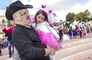 Beer-Sheva, İsrail-5 Mart 2015: Bıyıklı, siyah ve siyah kovboy şapkası şenlikli bir makyaj ile yaşlı bir adam ve küçük bir kız bir pembe elbise - Purim