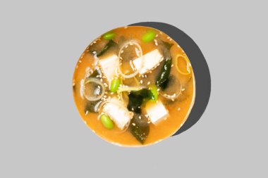 Gri arkaplanda kimchi çorbası izole edilmiş. Geleneksel Asya yemekleri. Tofu peyniri, pırasa, edamame fasulyesi ve yosun dolu sıcak baharatlı kimçi çorbası. Japon mutfağı. Restoran menüsü