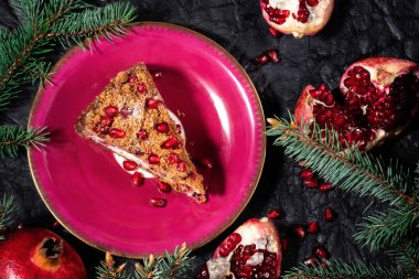 Siyah deri kumaş arka planında köknar dalları olan meyveli kek dilimi. Noel ya da Şükran Günü turtası ve fuşya renkli nar. Şenlikli masa dekorasyonu. Güzel peynirli kek tatlısı.