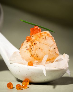 Gri arka planda kaşık halinde neşter. Kırmızı somon havyarı, daikon ve soğanla servis edilen kurutulmuş deniz tarağı. Kabuklu deniz ürünleri ve deniz ürünleri pişirme. Güzel yemek ya da suşi restoranı menüsü. Kapat.