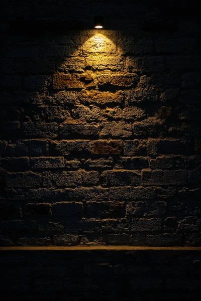 Dark room wall with ceiling light background. Old, weathered grey brick stone wall. Low key, scary, moody space. Room in basement. Vertical, copy space