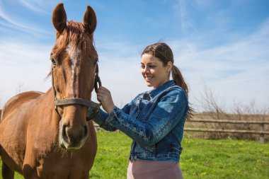 Happy beautiful brunette taking care of her brown horse
