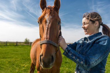 Happy beautiful brunette taking care of her brown horse 