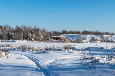 Karda kırmızı bir ev. Donmuş bir göletin arkasındaki ormanla çevrili.