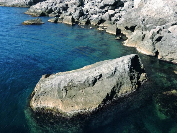 Tropikal bir ada mavi ve turkuaz berrak bir su ve ufukta mavi bir gökyüzü olan kayalık bir körfez kıyısı.          