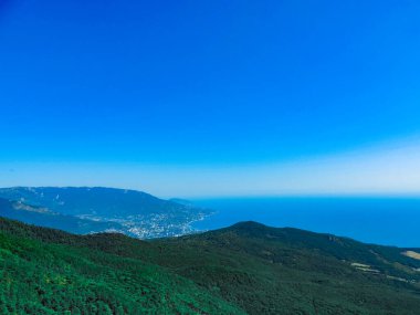 Mavi denizin ve açık gökyüzünün arka planında yeşil orman tepelerinin güzel manzarası.