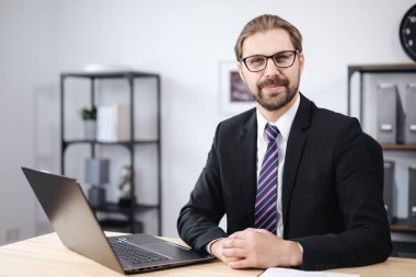 Gülümseyen adam dizüstü bilgisayarla masada oturuyor.