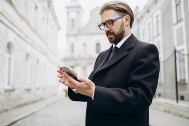 İş adamı sokakta akıllı telefon kullanıyor.