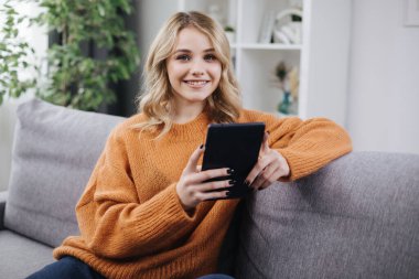 Kanepede tablet kullanan gülümseyen kadın.