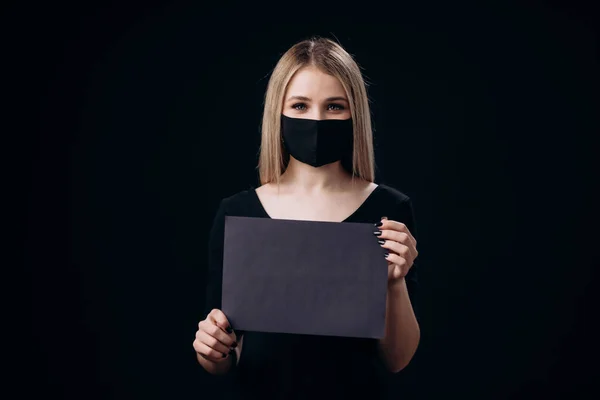 Блондинка в маске держит черную карту с пустым местом — стоковое фото